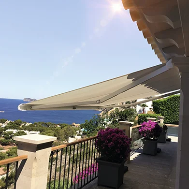Markise auf einer sonnigen Terrasse mit Blick auf das Meer und mediterrane Küstenlandschaft.